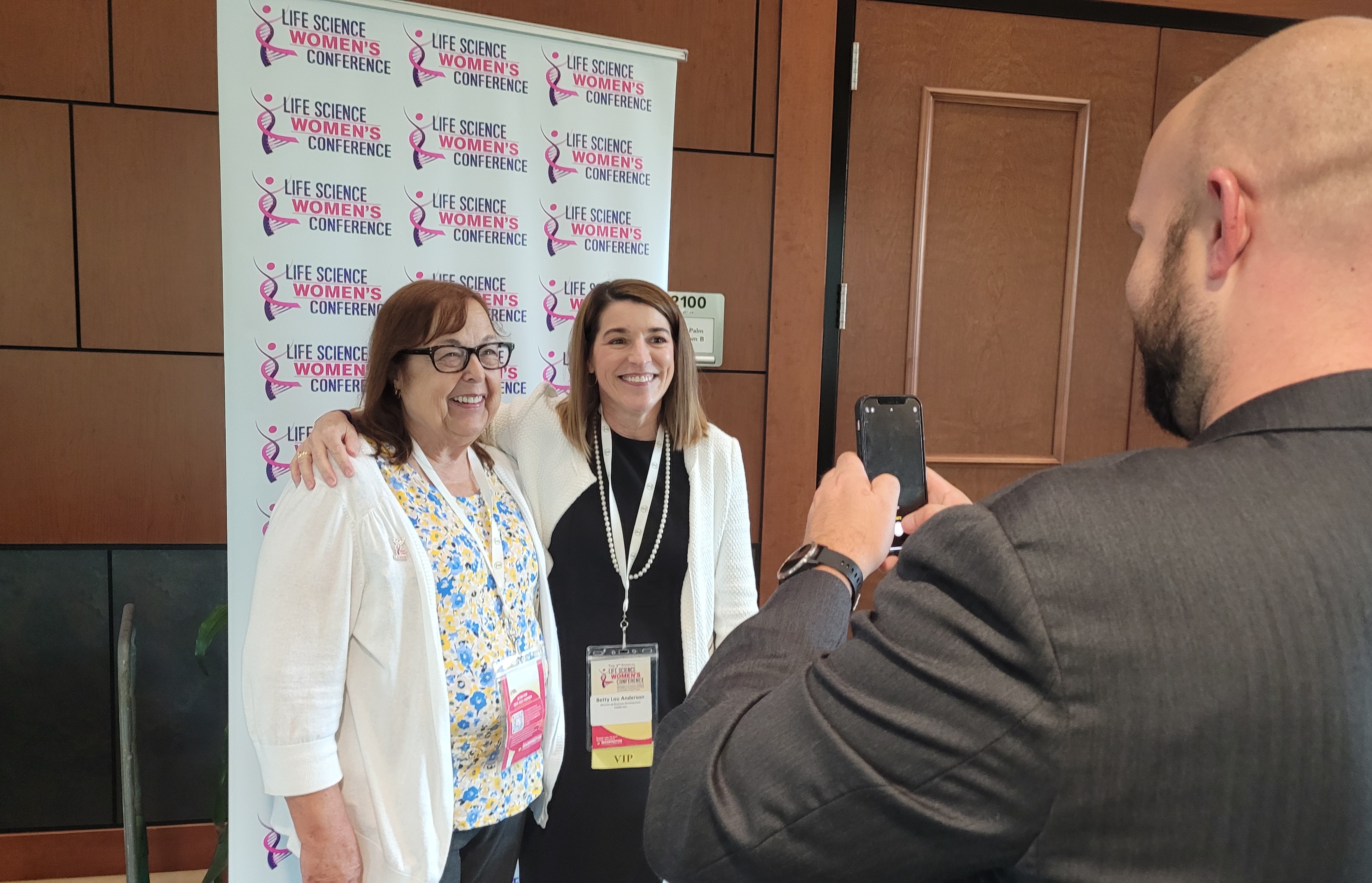 Attendees to the Life Science Women's Conference pose against a logo backdrop, smiling brightly.