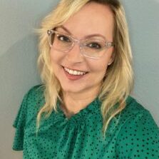 Catherine Marten, with shoulder-length blonde hair, a bright green top dotted with black, and clear square glasses.