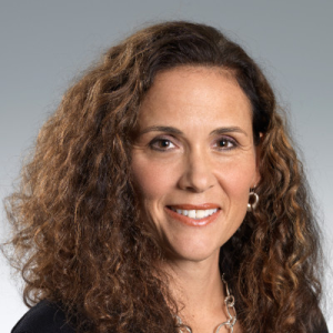 Kathleen's headshot. Curly, dark hair flows down to her shoulders, covered in black professional attire. Her smile is soft and professional.