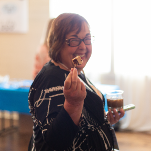 Co-founder Patti Rossman smiling at the camera, holding up a small piece of cake on a fork.