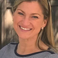 A headshot of Tina Parker. She's white, has long blonde hair, and is smiling brightly in a professional top, sunglasses atop her head.