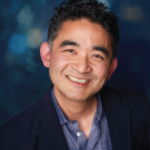 Ken Shitamoto, smiling brightly, with a blue background.