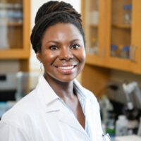 A headshot featuring Dr. Renee Cottle, hair up in a bun, smiling brightly as she wears her lab coat.