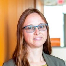 A headshot of Verena Kallhoff, smiling. She wears glasses and has shoulder-length brown hair.