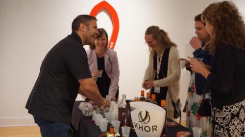 A group of people smiling and laughing over an exhibitor's booth at Chocolate Decadence, enjoying chocolate win and beer.